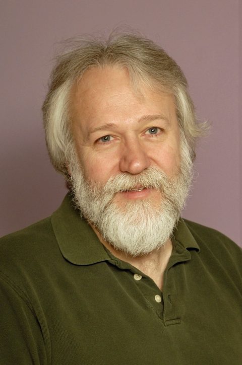 Portrait of Donald Bowman smiling, with gray hair, a white beard, and a dark green polo shirt.